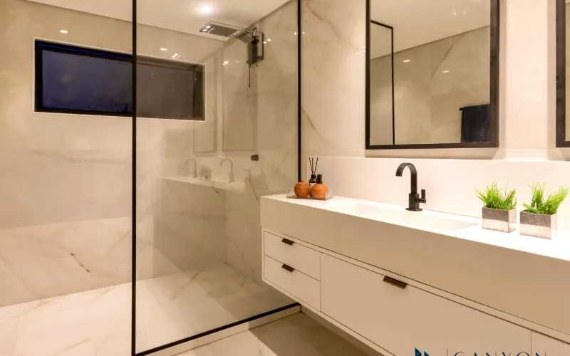 Modern bathroom with large glass-enclosed shower, white floating vanity with black faucet, two potted plants, and a wall mirror—perfect inspiration for your contractor for bathroom remodeling.