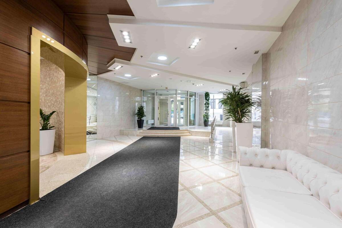Modern office lobby with marble floors, white sofa, potted plants, and glass entrance doors; wood and gold accents on the walls showcase stunning multifamily lobby transformations.