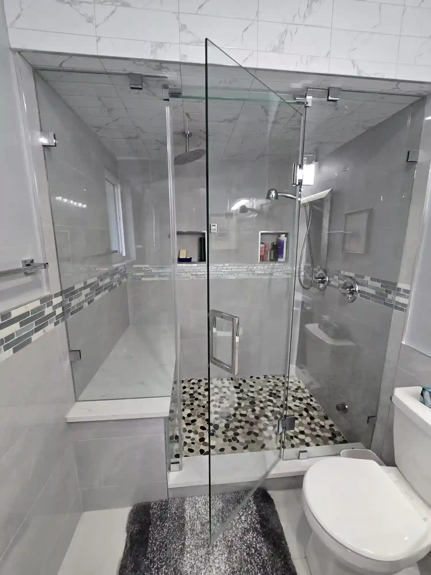 Modern bathroom with a glass-enclosed shower featuring a rainfall showerhead, built-in bench, mosaic tile floor, and a toilet next to the shower area—perfect inspiration if you're considering commercial kitchen remodeling too.