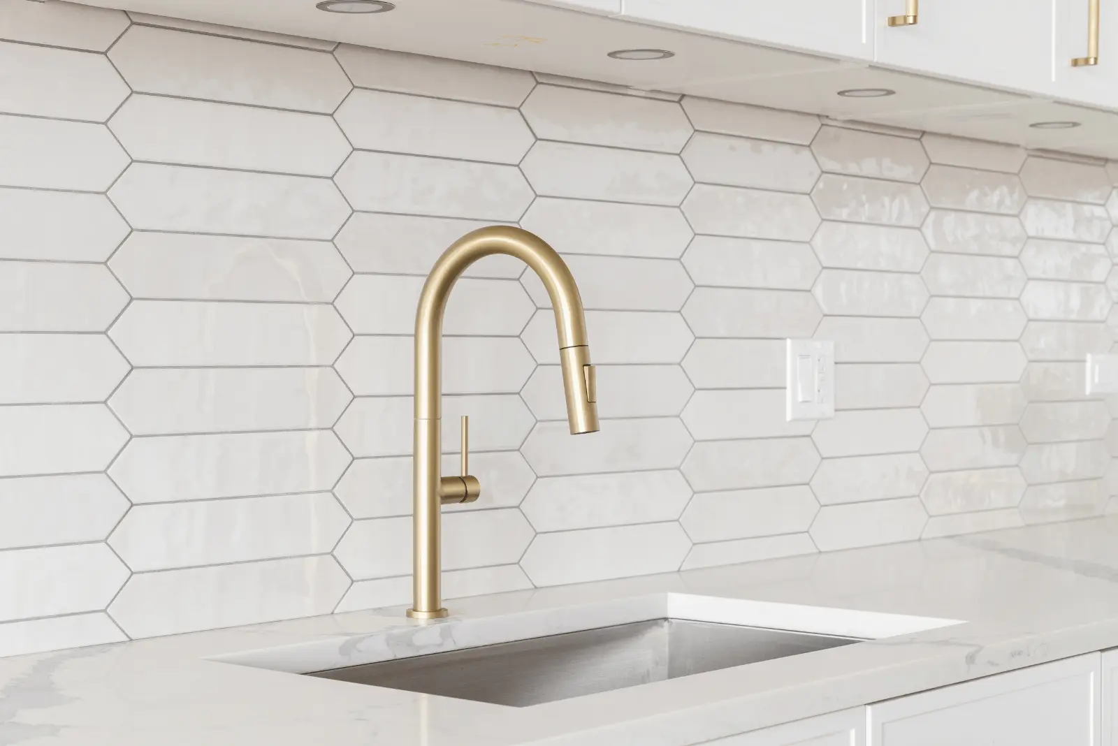 A modern kitchen sink with a gold faucet set against a white hexagonal tile backsplash and white countertop.