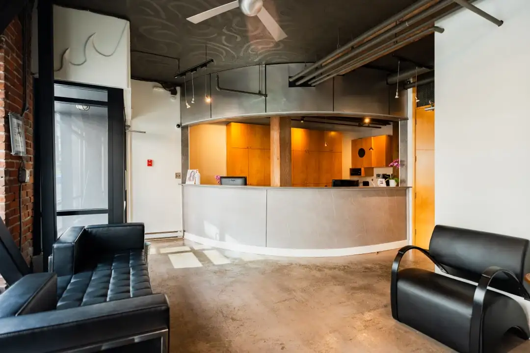 Modern reception area featuring a curved front desk, black leather seating, exposed brick wall, and industrial-style ceiling and lighting—perfect inspiration for office renovations Canada.