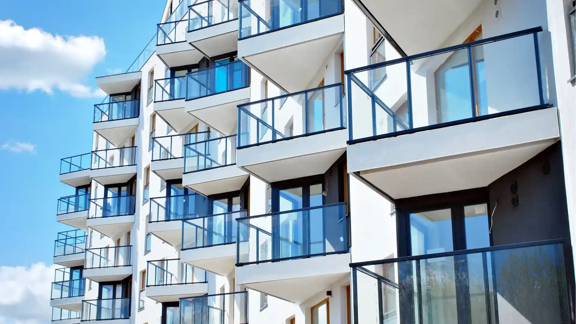 Modern apartment building with multiple floors, white exterior, and glass balconies, photographed from an upward angle against a blue sky and featuring custom stair railings Canada for a contemporary touch.