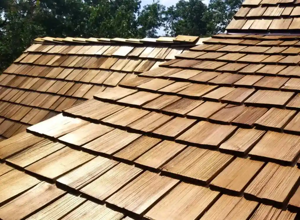Close-up view of a wooden shingle roof with overlapping panels, illustrating the craftsmanship often sought during roof replacement, set against a background of trees and blue sky.