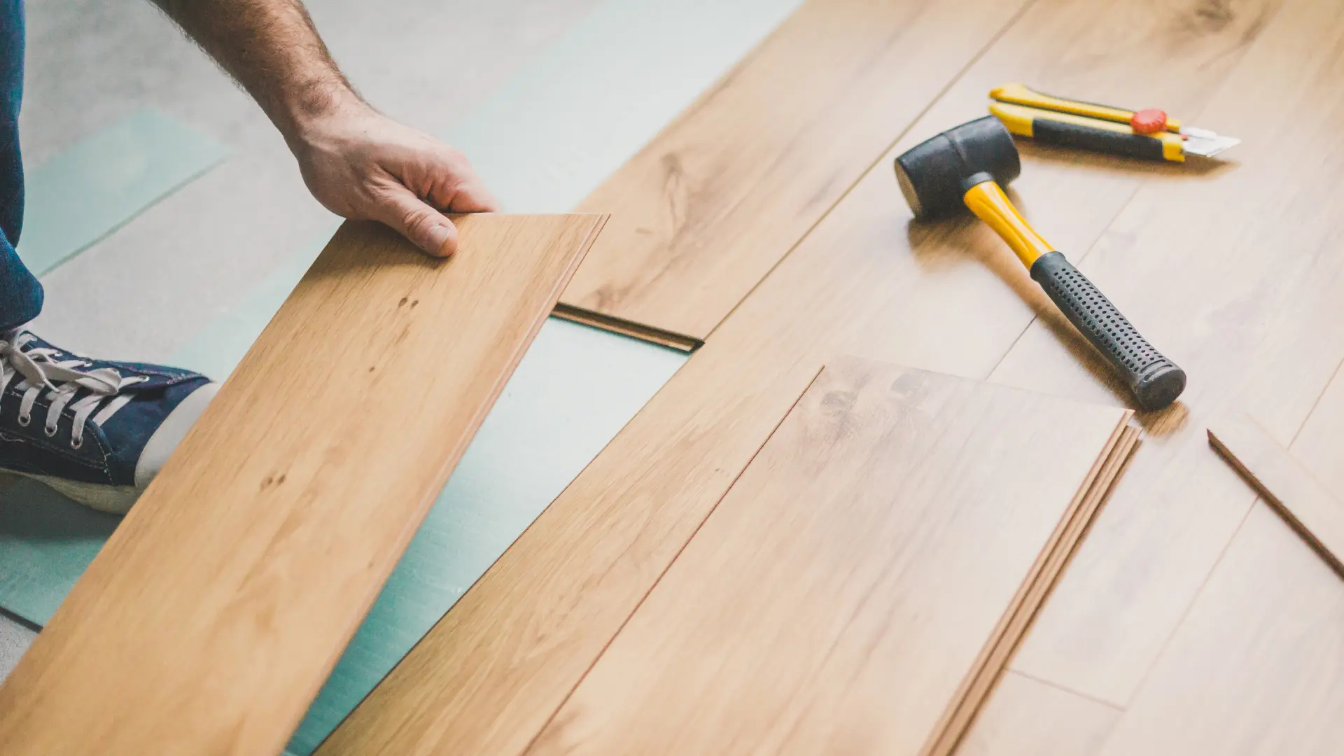 In Abbotsford, a person installs wooden laminate flooring with a rubber mallet and tools nearby, ensuring every detail is perfect before the upcoming pipe replacement.