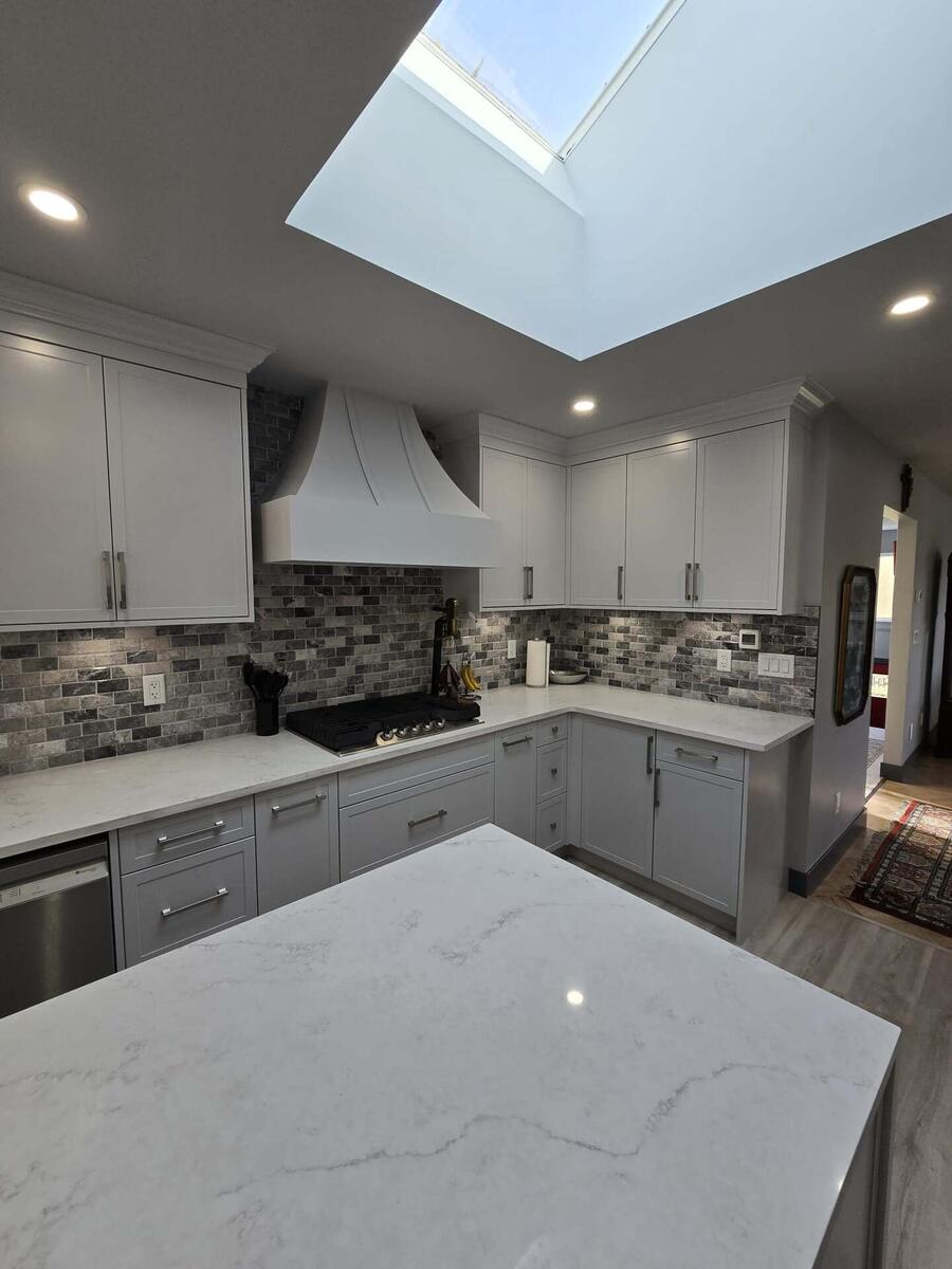Modern kitchen with white cabinets, marble countertops, gray tile backsplash, stainless steel appliances, and a skylight providing natural light—designed for easy property maintenance and lasting appeal.