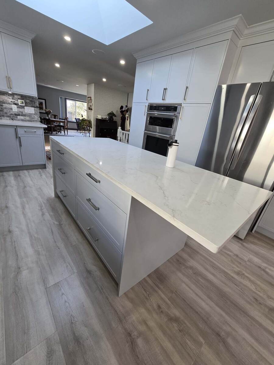 Modern kitchen with light gray cabinets, large marble island, stainless steel appliances, and light wood flooring; a white water bottle sits on the island, showcasing the care and attention to property maintenance throughout.