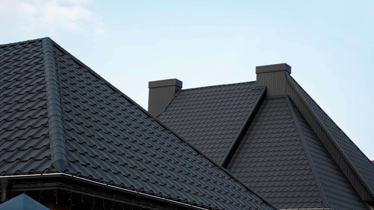 Image of a residential house with dark gray metal roofing and two prominent chimneys against a clear sky.